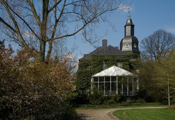 Außenaufnahme, Wintergarten und Efeubewachsung am Schloss Styrum. Im Vordergrund Bäume und Sträucher.