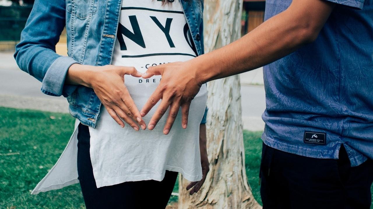 Junges Paar erwartet ein Baby. Der Mann streicht der Frau über den Bauch.