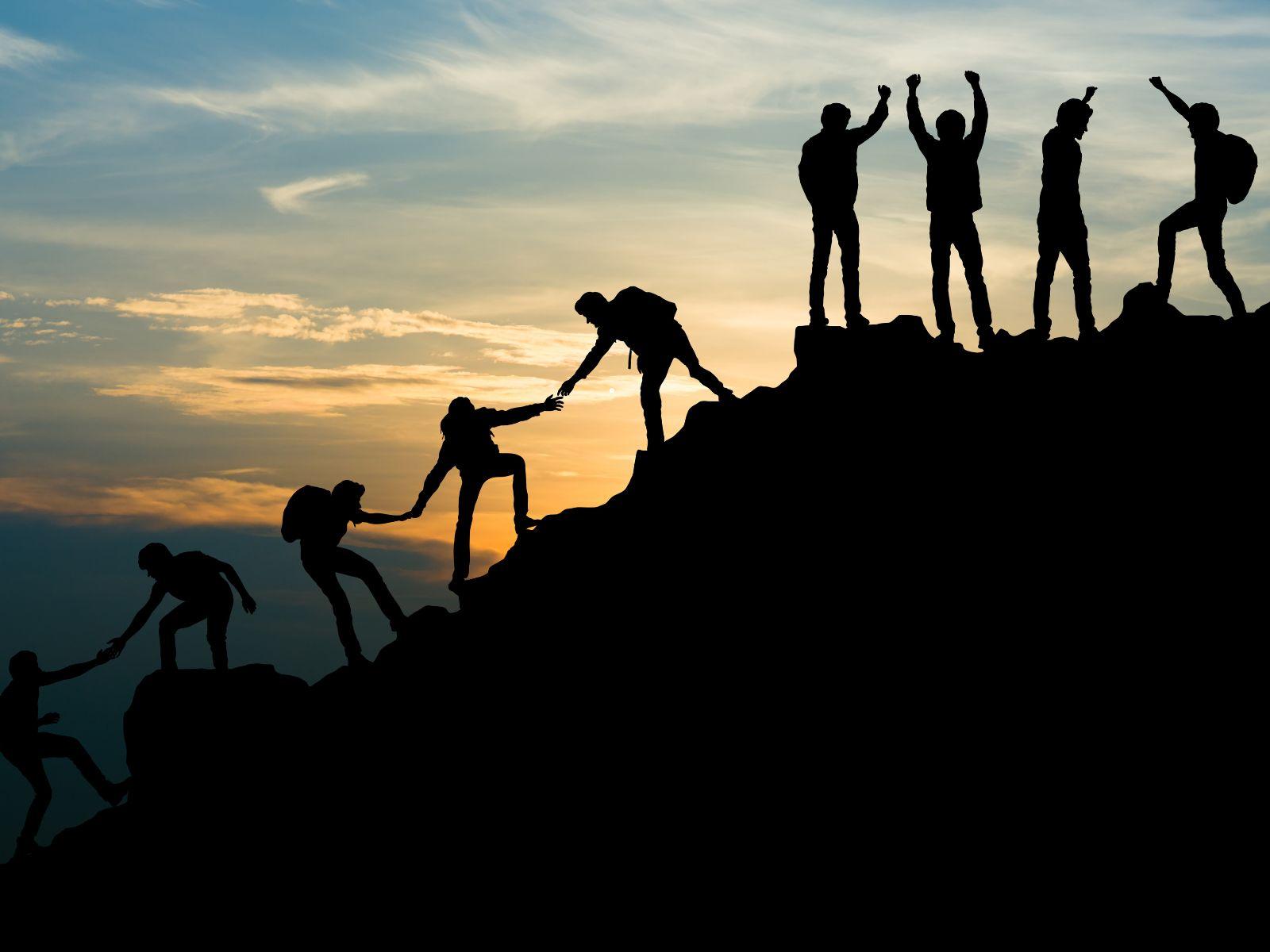 Eine Gruppe von Menschen besteigt einen Berg. Sie helfen sich untereinander die Bergspitze zu erreichen.