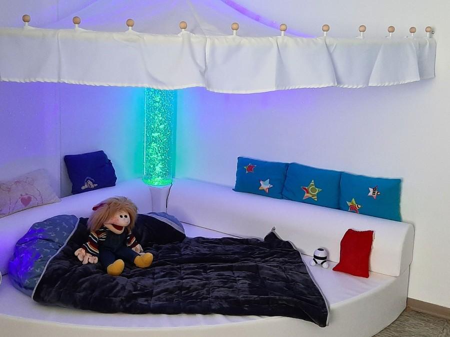 Eine Kuschelecke mit einer Lavalampe, Kissen und einer Decke lädt zum Entspannen ein.