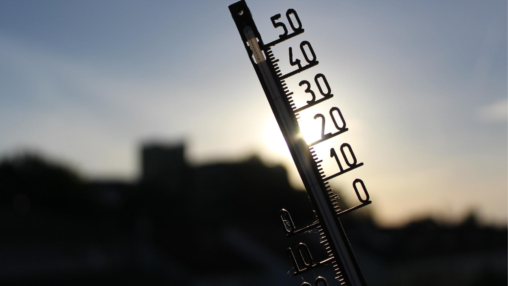 Im Vordergrund ein Thermometer, im Hintergrund ein Sonnenuntergang.