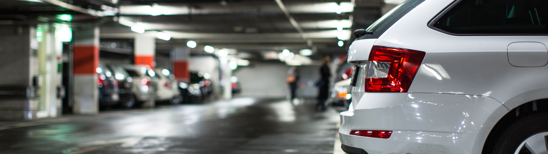 Eine Tiefgarage mit mehreren parkenden Autos und im Hintergrund zwei Personen, die nur unscharf zu sehen sind.