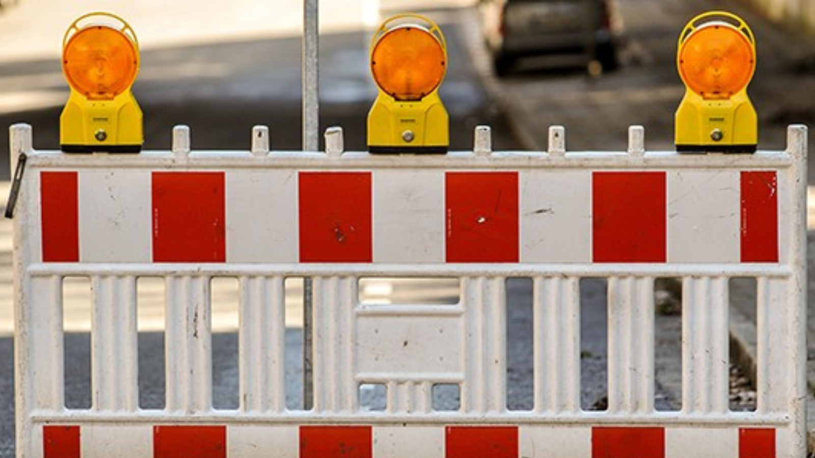 Absperrung mit rot-weißen Streifen und drei gelben Warnleuchten auf einer Straße