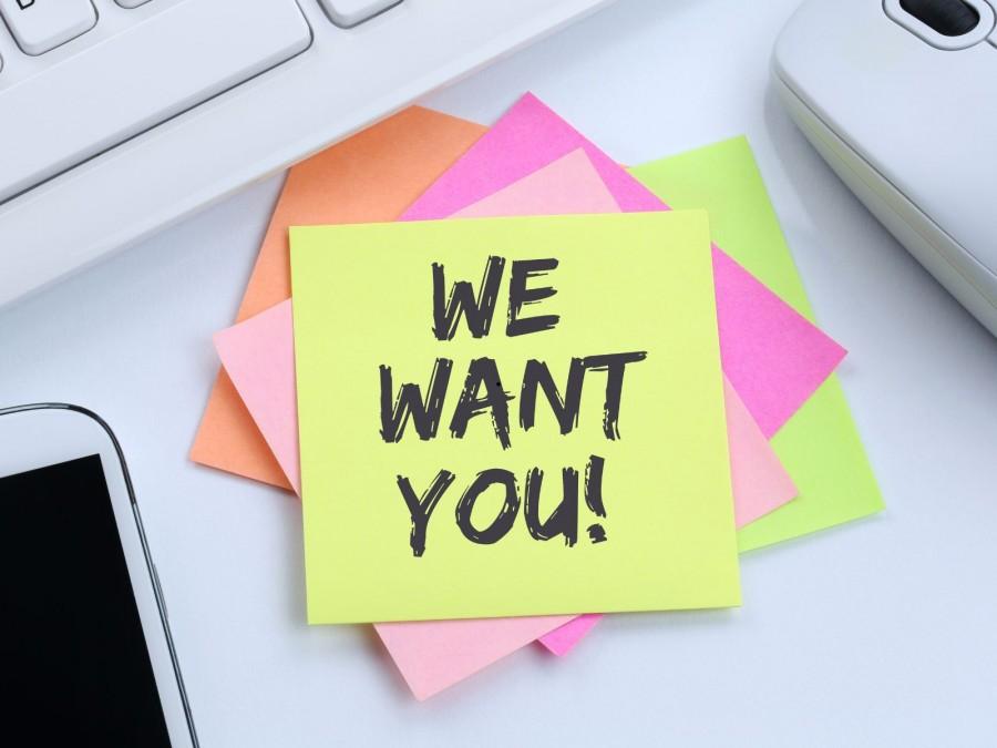 Mehrere bunte Klebezettel liegen übereinander auf einem Schreibtisch. Auf dem oberen Zettel steht We want you!