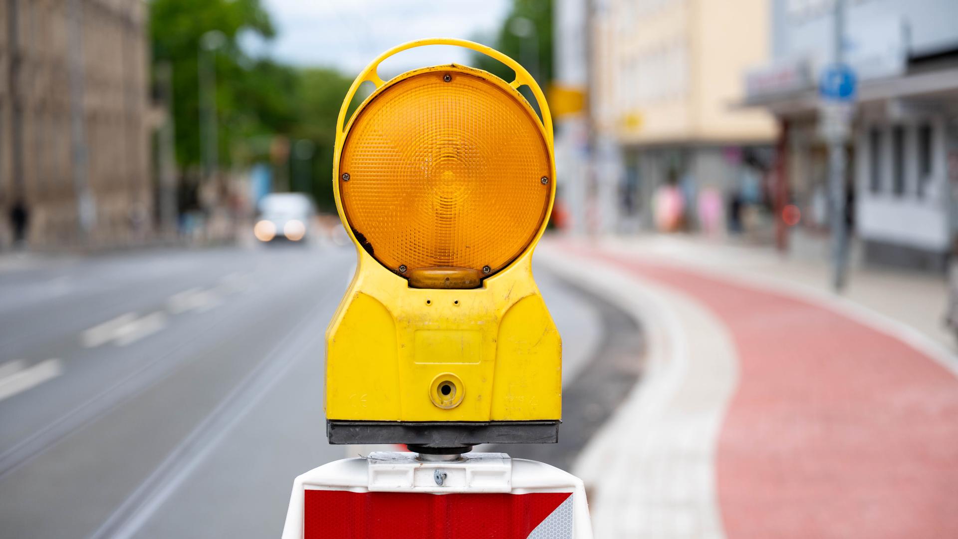 Gelbe Warnleuchte an Baustelle auf Fahrradweg, unscharfe Stadtstraße im Hintergrund