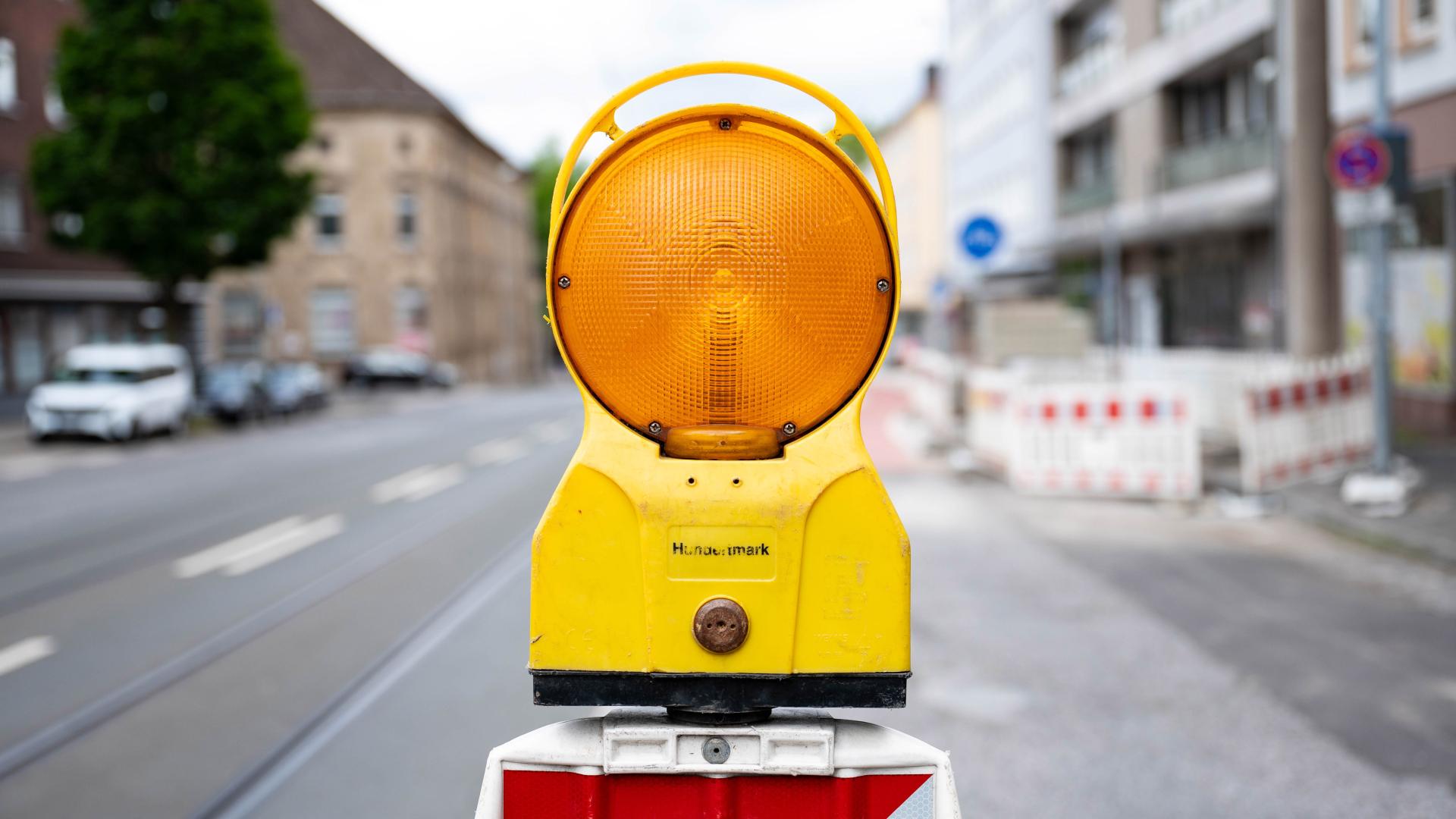 Gelbe Warnleuchte an Baustelle auf Fahrradweg, unscharfe Stadtstraße im Hintergrund
