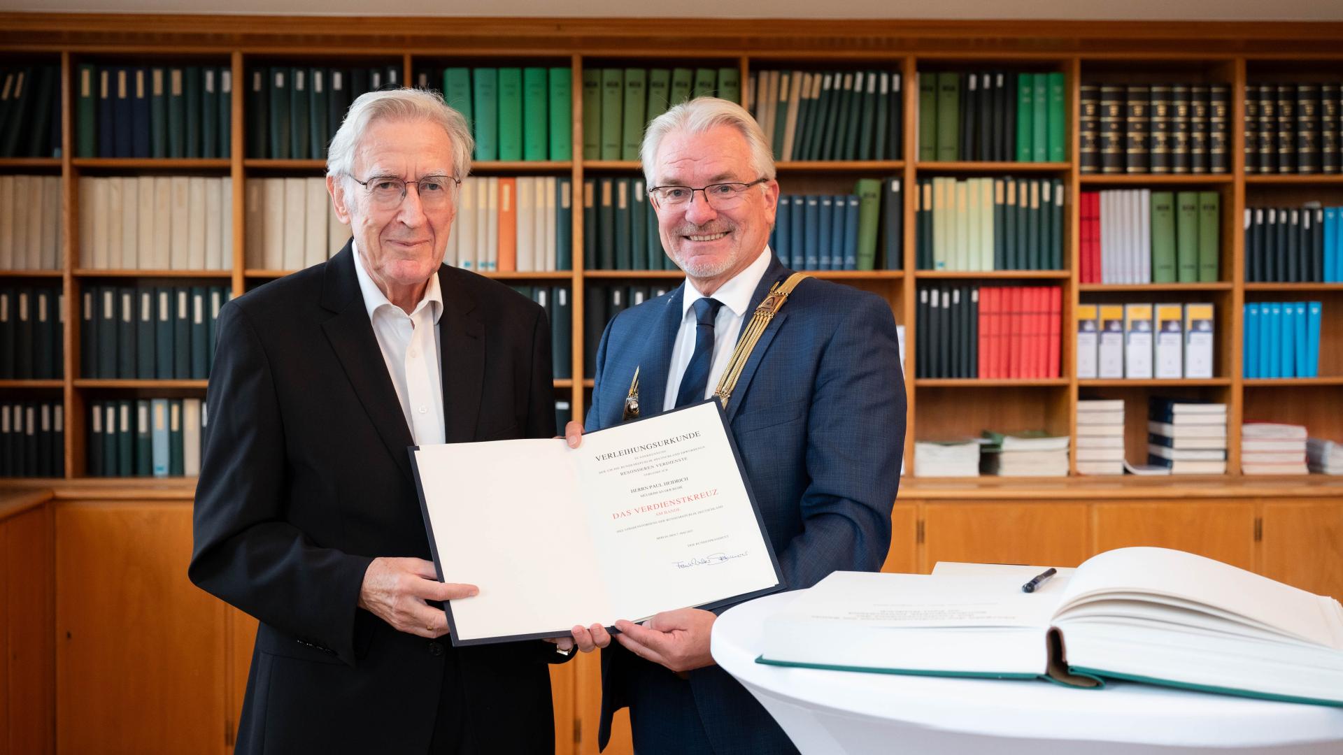 Paul Heidrich, Träger des Bundesverdienstkreuzes am Bande, steht neben Oberbürgermeister Marc Buchholz. Beide halten eine Urkunde in der Hand.