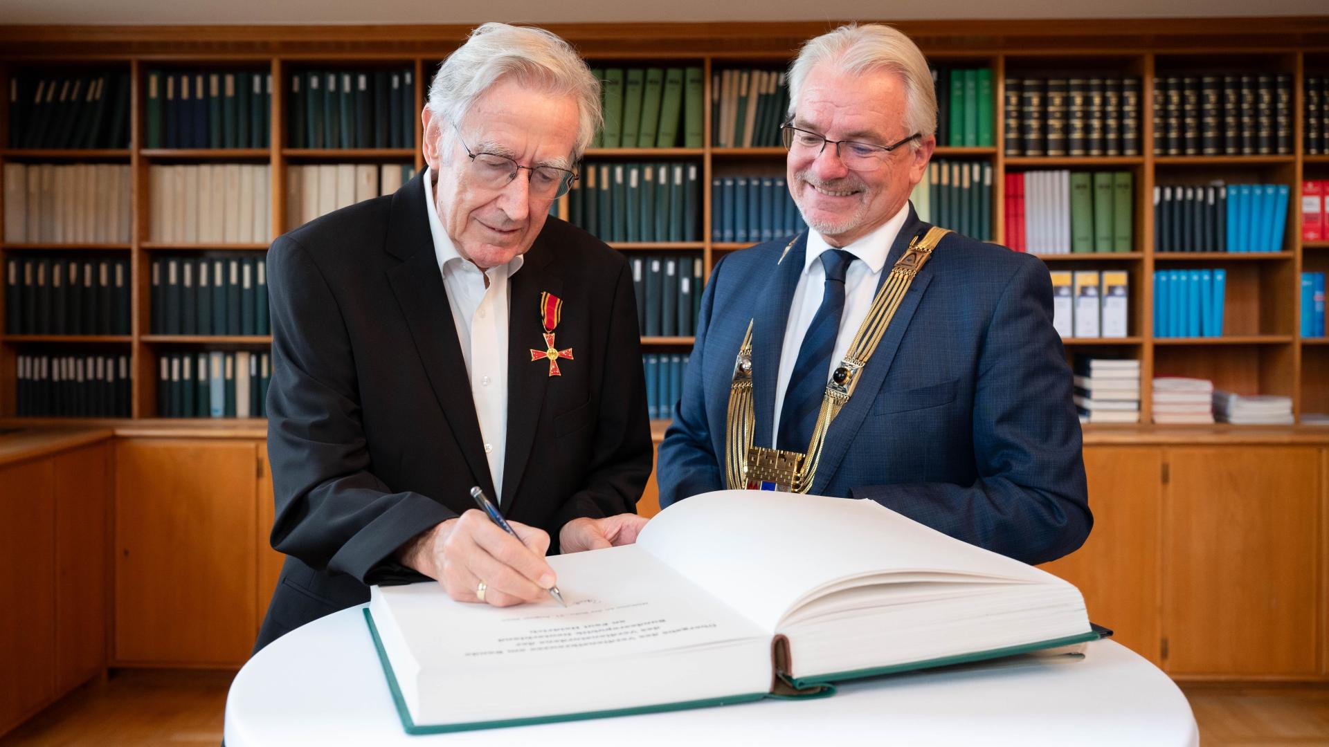 Paul Heidrich, Träger des Bundesverdienstkreuzes am Bande, steht neben Oberbürgermeister Marc Buchholz ein und trägt sich ins Gästebuch der Stadt Mülheim an der Ruhr ein.