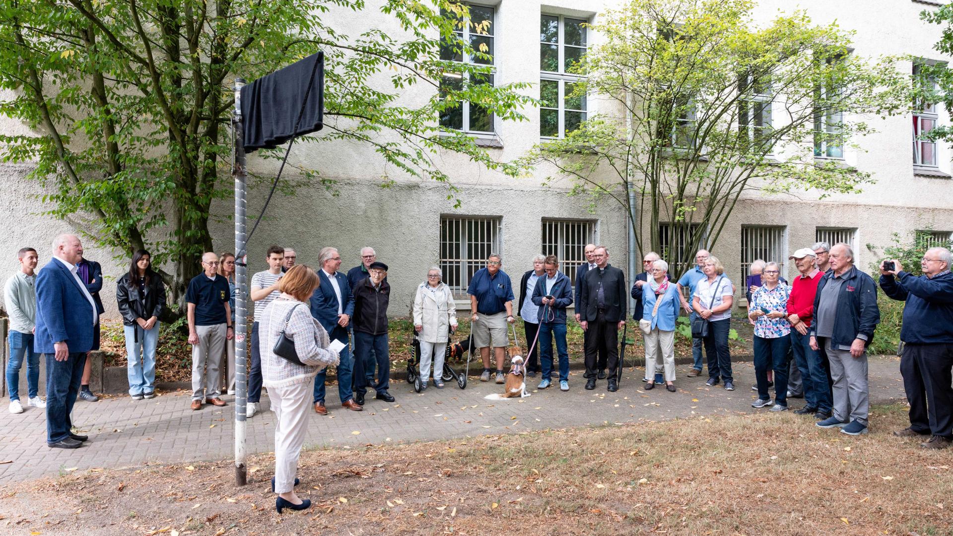 Menschen stehen vor dem verhüllten Straßenschild des Heinrich-Mühlsiepen-Parks