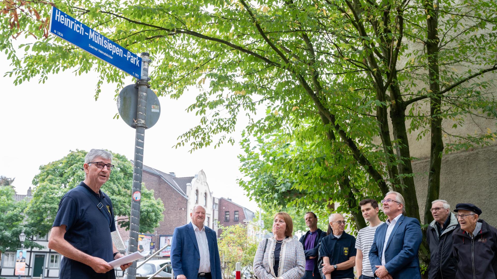 Menschen stehen vor dem neuen Straßenschild des Heinrich-Mühlsiepen-Parks, ein Mann hält eine Rede