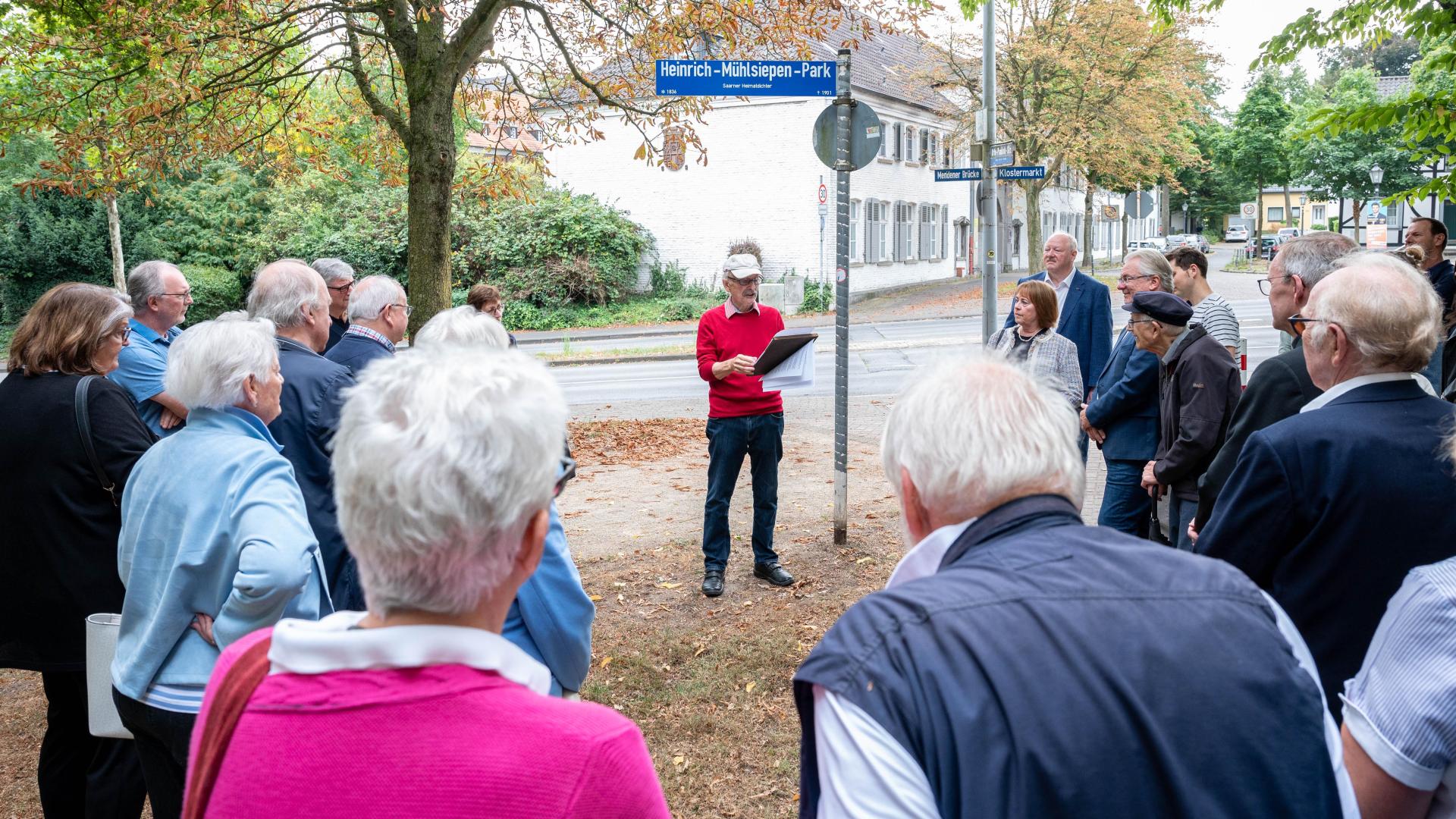 Menschen stehen vor dem neuen Straßenschild des Heinrich-Mühlsiepen-Parks, ein Mann hält Rede