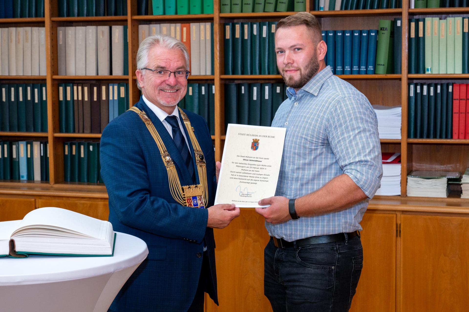 Oberbürgermeister Marc Buchholz übergibt in der Rathausbibliothek eine Urkunde an Oliver Schmidthaus.