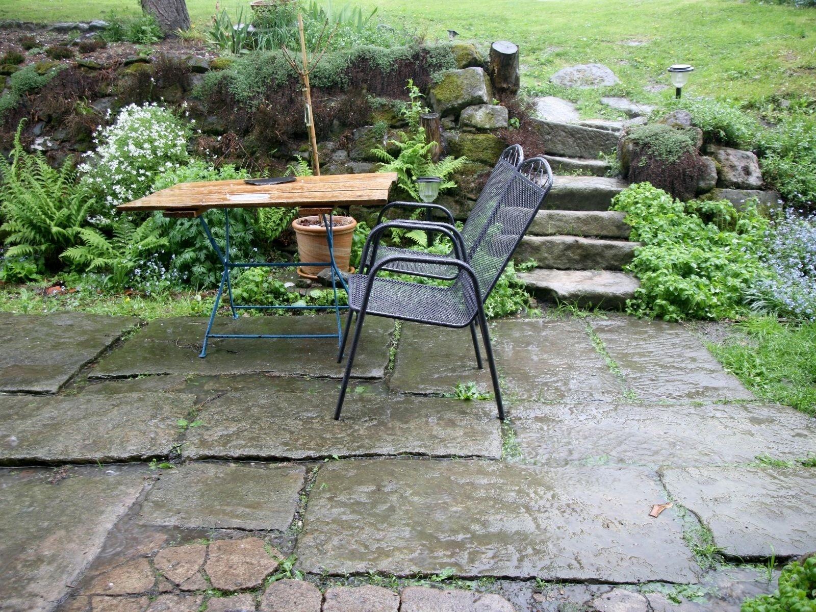 Blick durch den Regen auf eine Terrasse mit Tisch und Stühlen.