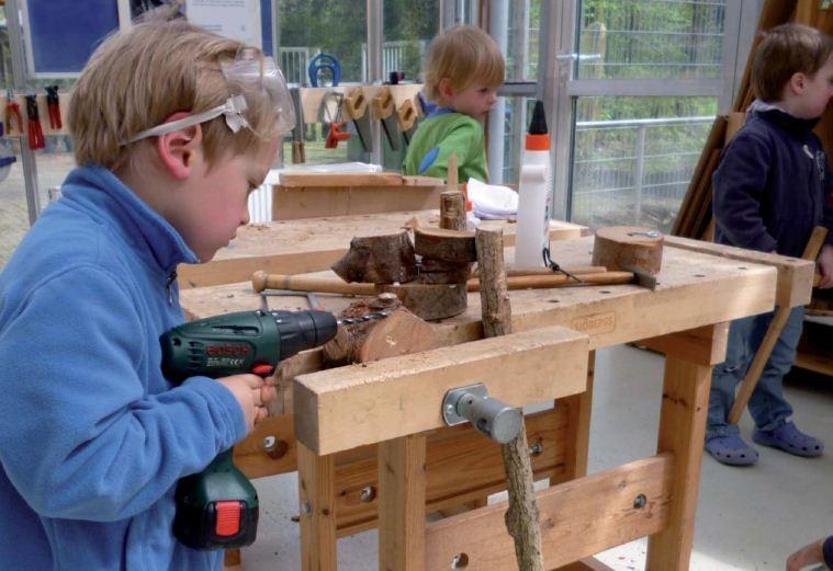 Kleiner Junge an einer Werkbank, arbeitet mit einer Bohrmaschine, Lernwerkstatt Natur