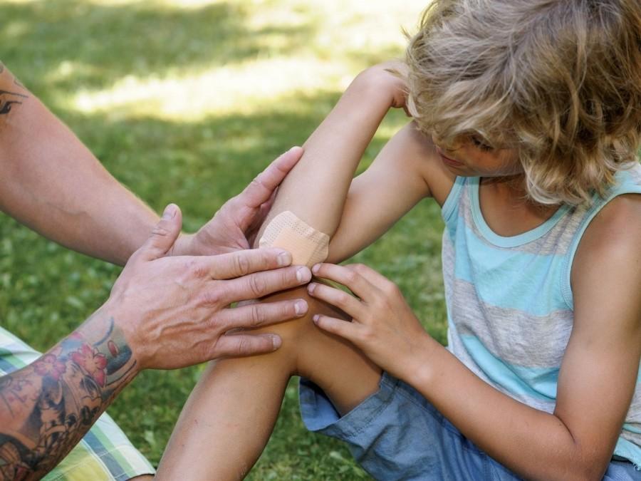 Tagespflegeperson hat eine leichte Verletzung eines Kindes am Ellbogen versorgt und ein Pflaster darauf klebt. Notfall, Gefährdungsbeurteilung.
