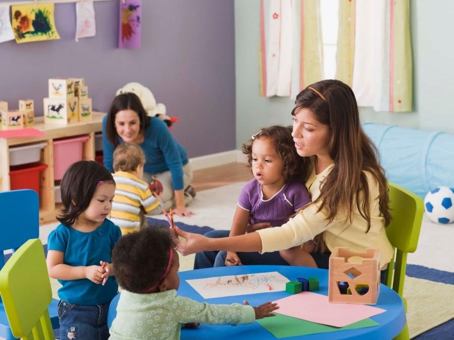 Zwei Tagespflegepersonen spielen mit Kleinkindern im Tagespflegenest. Kindertagespflegepersonen, Kita, Kindergarten, Kinderbetreuung, Pflegevater, Pflegemutter.
