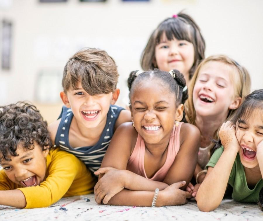 Kinder liegen neben- und übereinander auf dem Boden, lachen und freuen sich. Tagespflegenest, Kita, Kindergarten, Kinderbetreuung, Pflegevater, Pflegevater, Kindertagespflege.