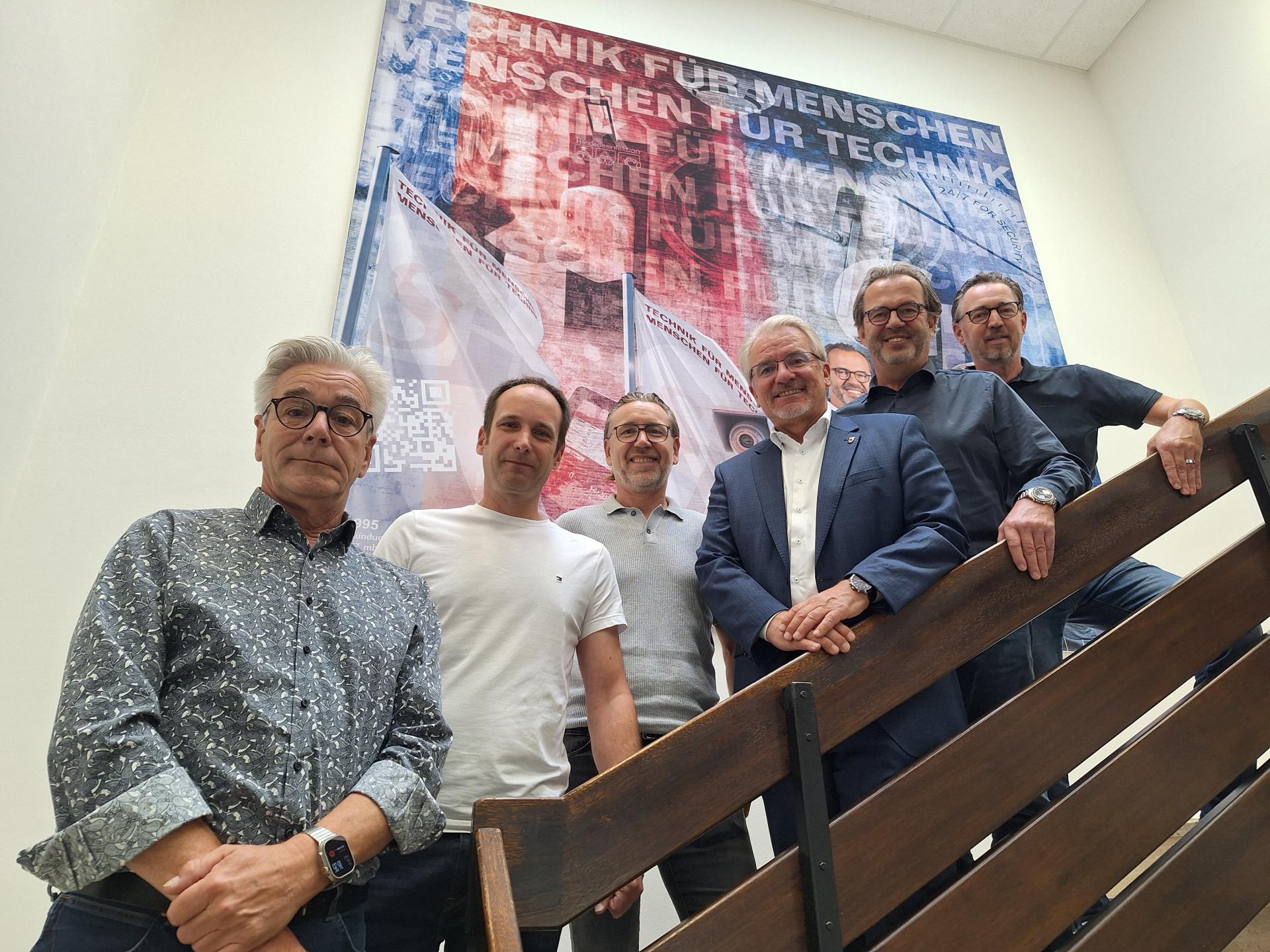Oberbürgermeister Marc Buchholz steht mit Mitarbeitern der Firma GST Gesellschaft für Sicherheitstechnik mbH auf einer Treppe.