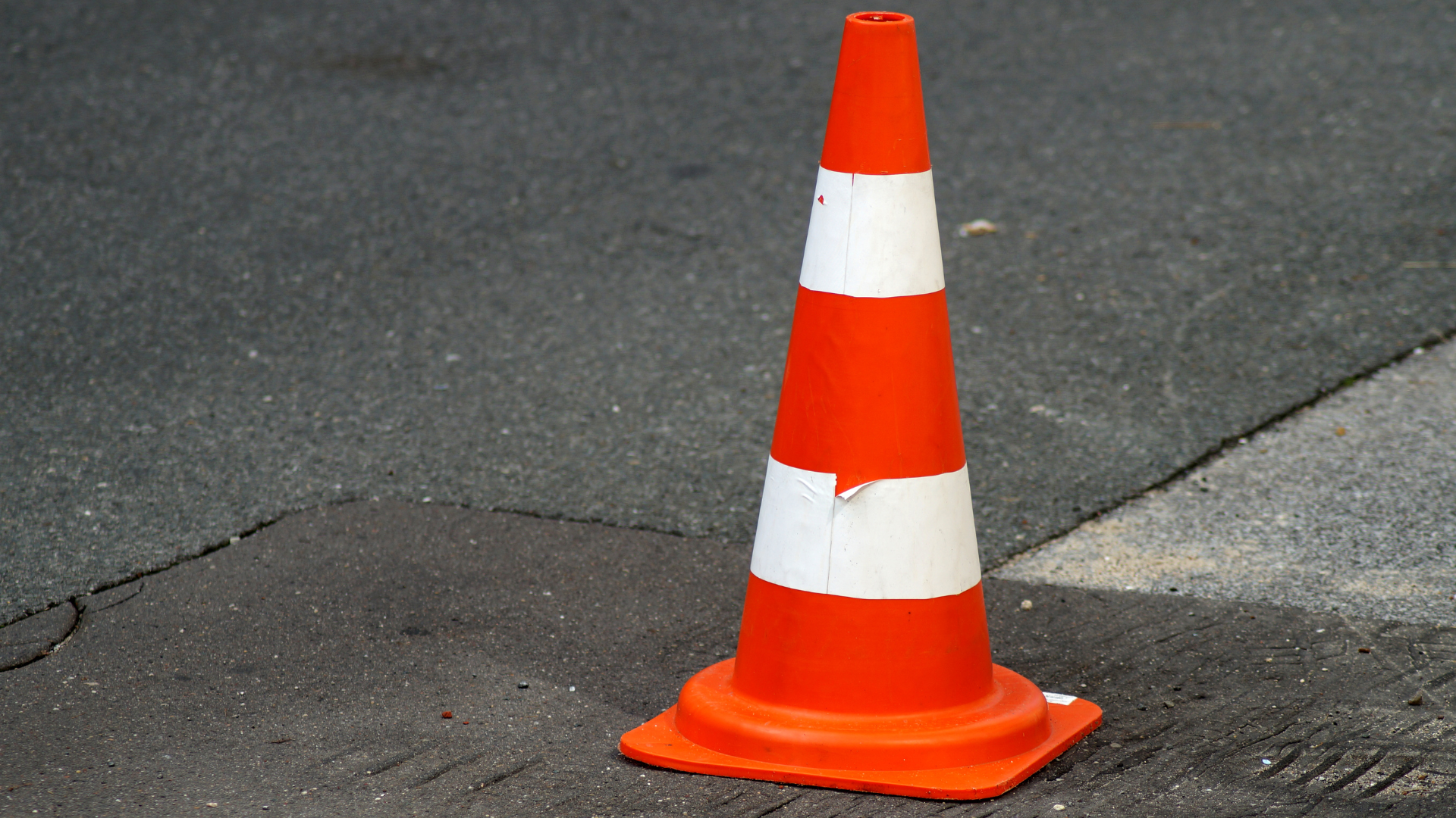 Eine orange-weiß gestreifte Pylone steht auf der Straße.