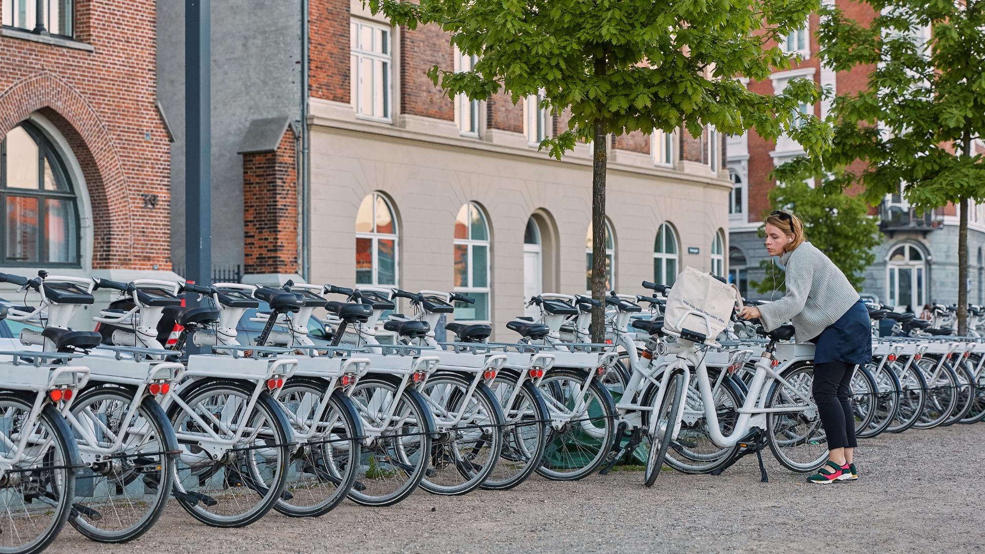 Eine Frau löst in einer Reihe von Leihfahrrädern ein Fahrrad.
