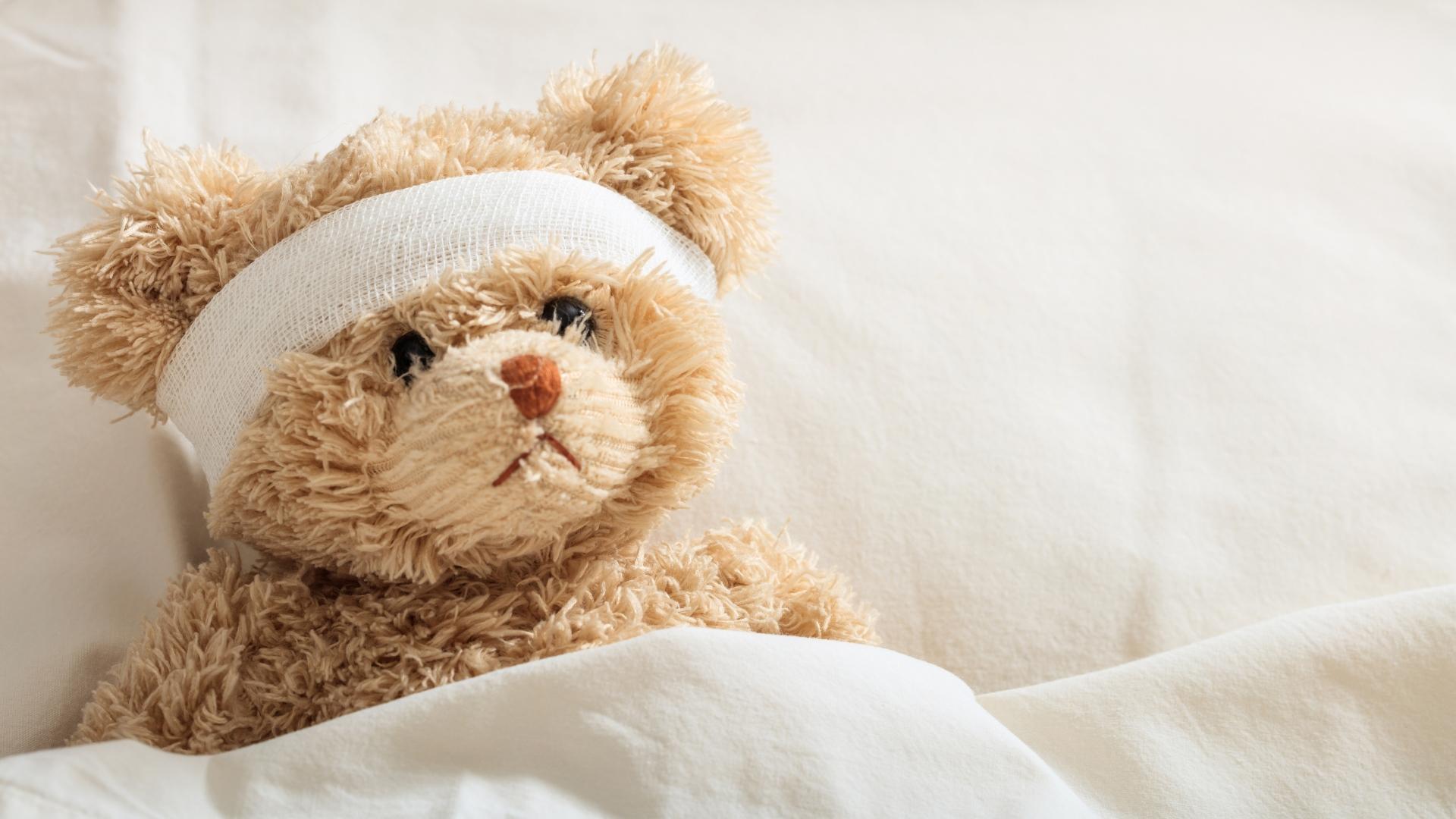 Teddy Bär mit Verband welcher im Bett liegt