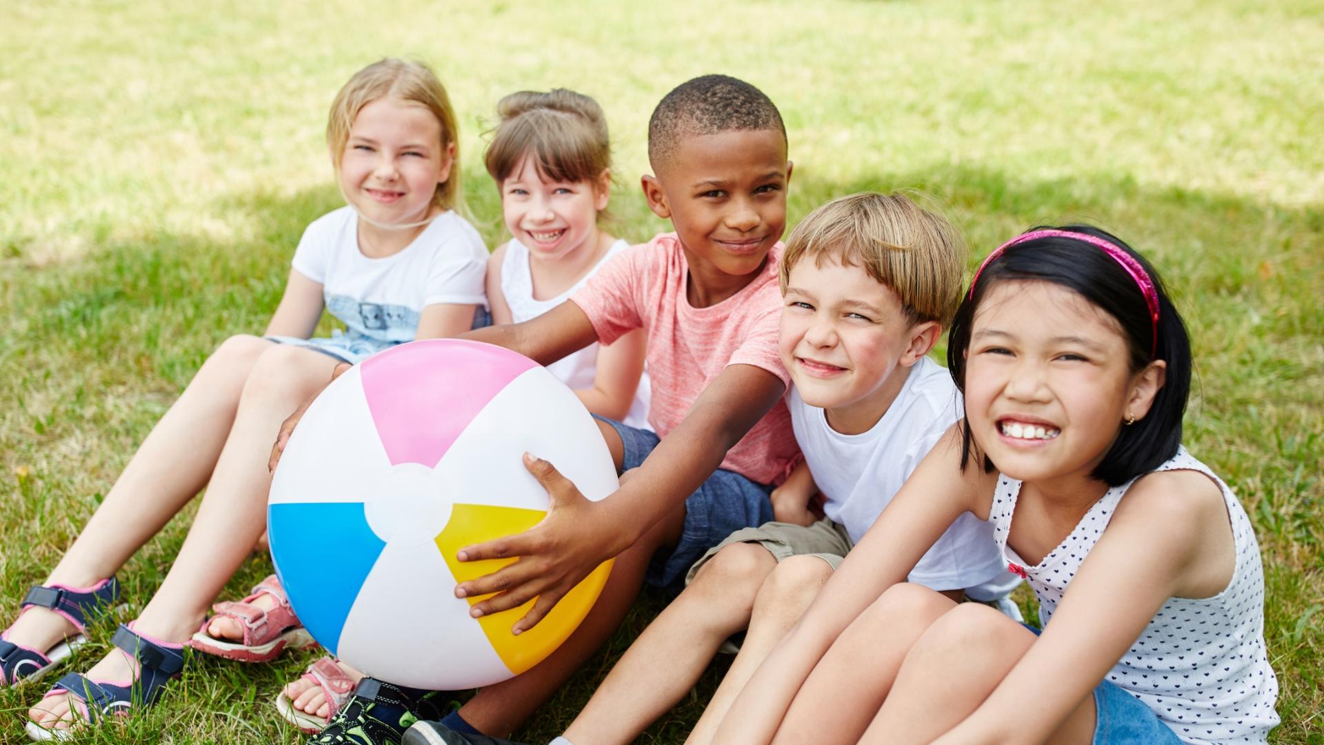 fünf Kinder verschiedener Nationalitäten sitzen nebeneinander und halten einen großen Ball in den Händen