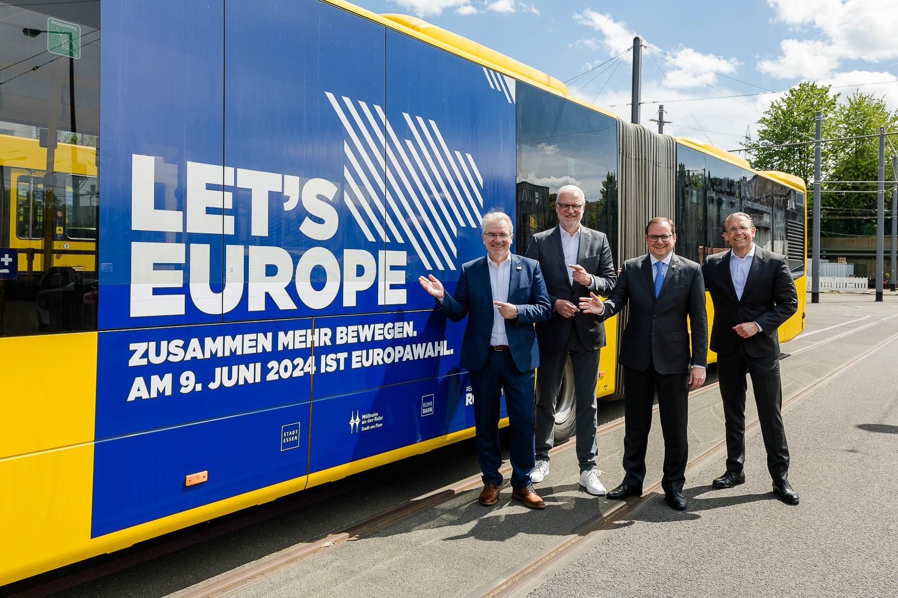 vier Männer stehen vor einem Bus und zeigen auf die Aufschrift "Lets Europe"