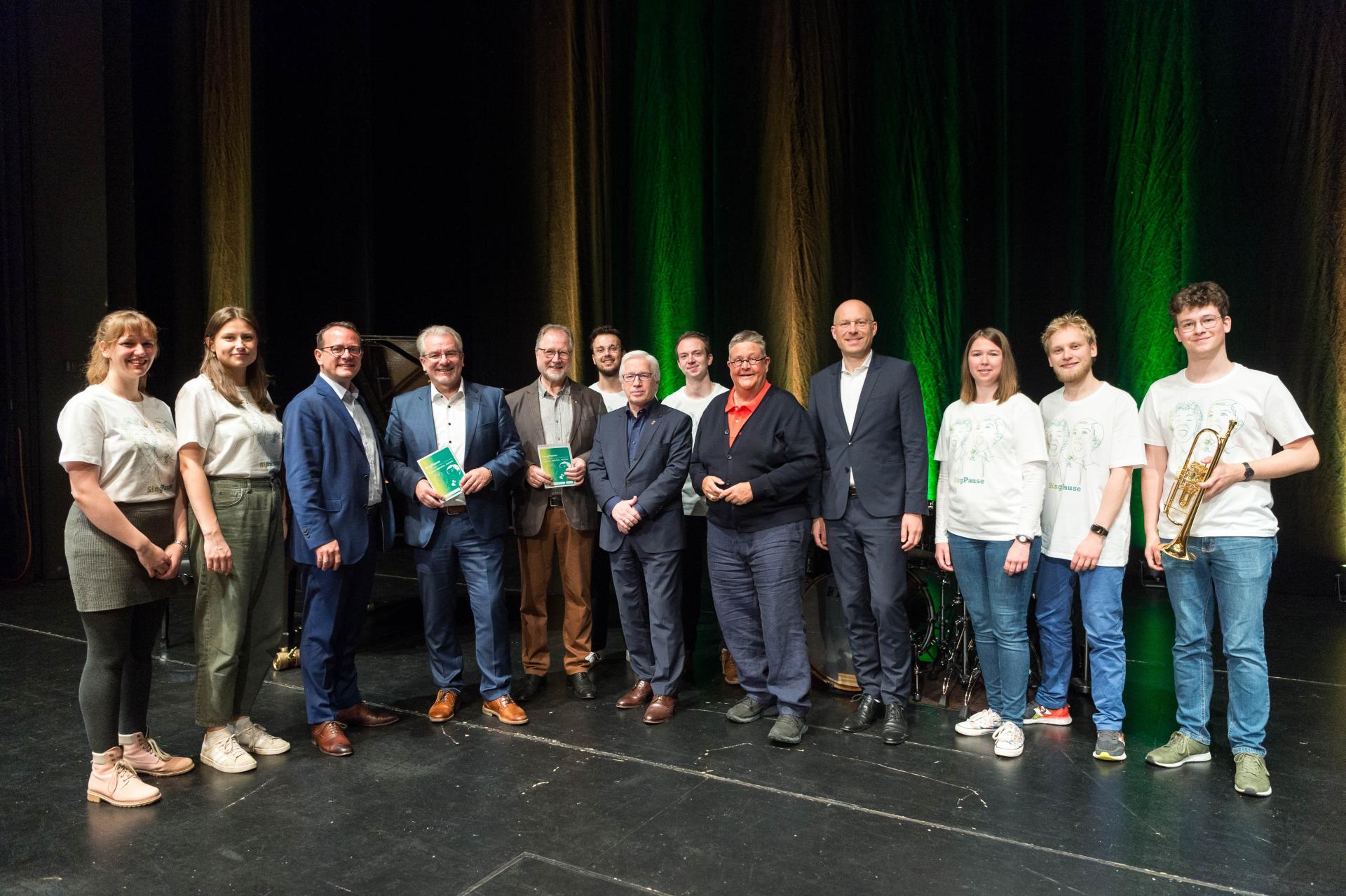 von links: Singleiterinnen Jana Stradmann und Anja Vogelsberger, Stadtdirektor und Schuldezernent David A. Lüngen, Oberbürgermeister Marc Buchholz, Projektleiter Professor Werner Schepp, dahinter: Singleiter Felix Kaumanns und Musiker der Jungen Kantorei Himmelfahrt, vorne: Stadtkämmerer Frank Mendack, Kulturdezernentin Doktor Daniela Grobe, Beigeordneter Felix Blasch, Singleiterin Leandra Binder, Musiker der Jungen Kantorei Himmelfahrt