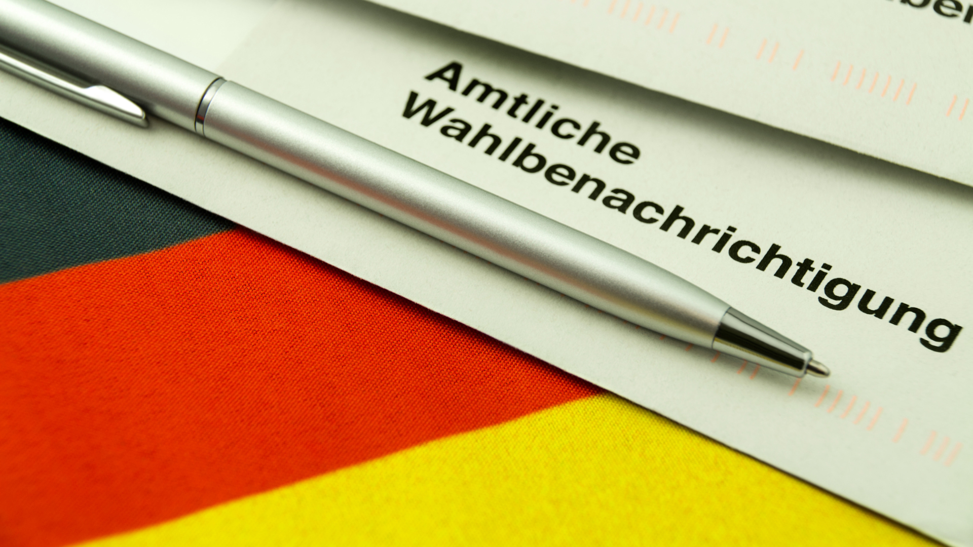 Im Hintergrund befindet sich eine Deutschland Flagge. Im Vordergrund eine Amtliche Wahlbenachrichtigung und ein Kugelschreiber
