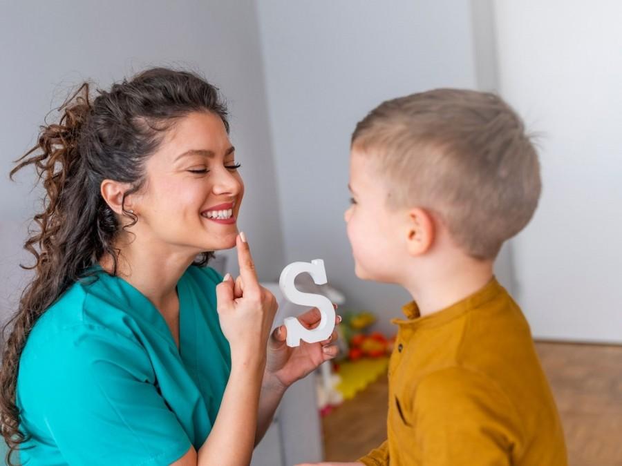 Logopädin macht mit einem Kind Sprachübungen, im Bild das Beispiel des Buchstaben S. Tagespflegenest, Kita, Kindergarten, Kinderbetreuung, Pflegevater, Pflegemutter, Kindertagespflege.
