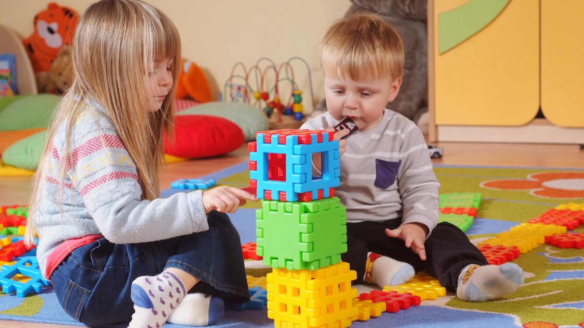 Kinder die auf dem Boden sitzen und mit Bausteinen spielen