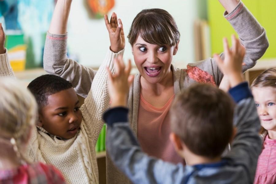 Tagespflegeperson spielt mit kleinen Kindern, alle heben die Hände in die Luft. Tagespflegenest, Kita, Kinderbetreuung, Pflegevater, Pflegemutter, Kindertagespflege.