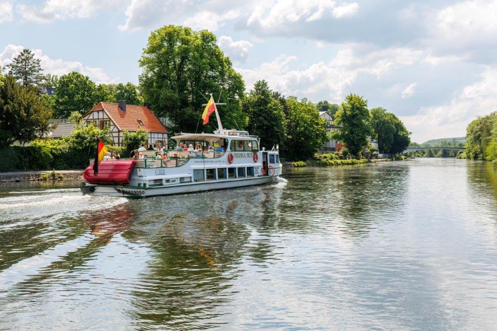 Auf dem Bild ist zu sehen wie das Fahrgastschiff Friedrich Freye an einem schönen Sommertag die Ruhr mit Fahrgästen Richtung Kettwig befährt.