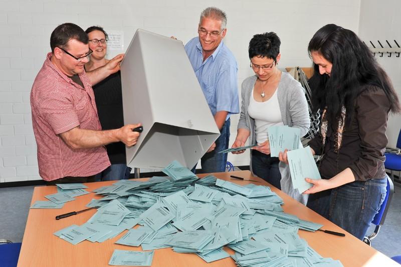 fünf Personen schütteln eine Wahlurne aus und verteilen die Wahlbriefe auf einem Holztisch