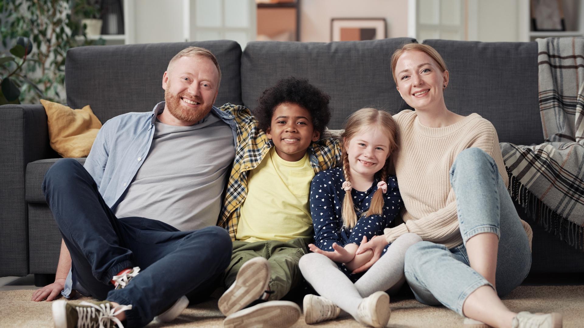 eine vierköpfige Familie sitzt glücklich vor der Couch, auf dem Teppich