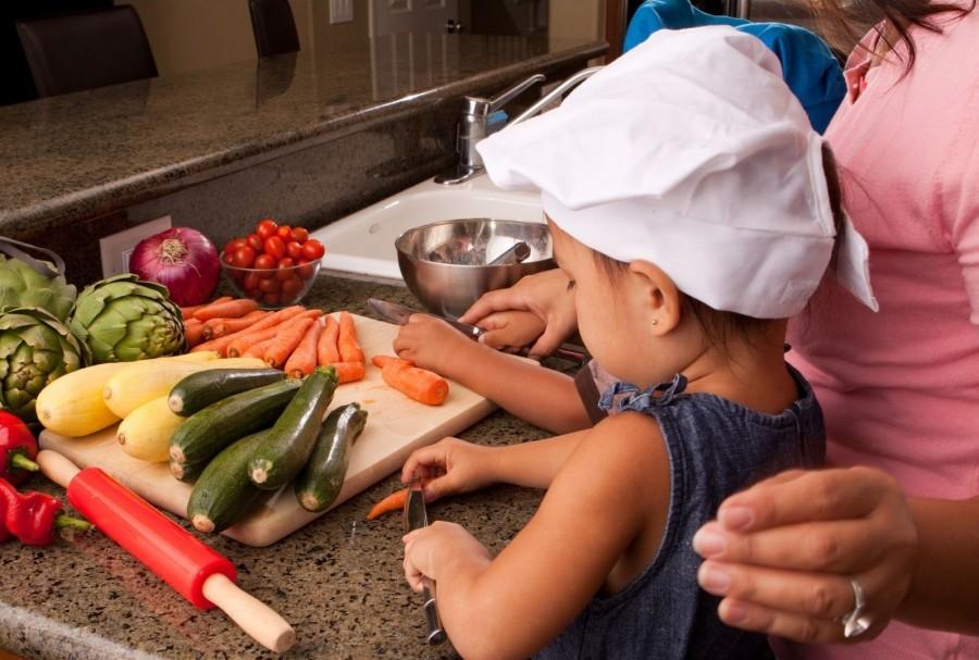 Kleines Kind kocht gemeinsam mit der Kindertagespflegeperson. Sie schneiden Karotten. Tagespflegenest, Kita, Kindergarten, Kinderbetreuung, Pflegevater, Pflegemutter, Kindertagespflege