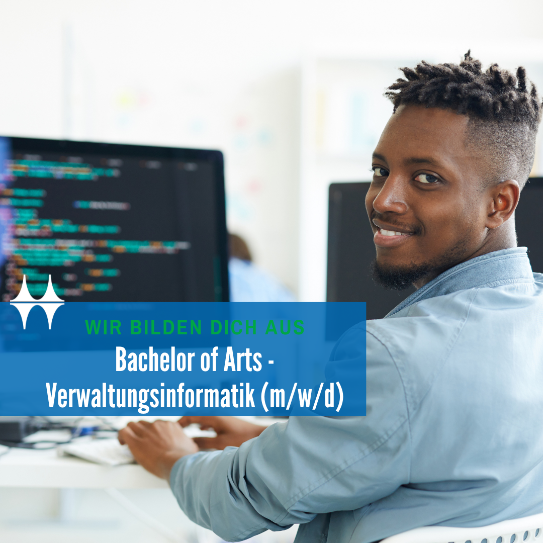 Das Bild zeigt einen jungen Mann sitzend an einem Tisch. Er dreht sich in die Kamera und lächelt. Auf dem Tisch steht ein Monitor und eine Tastatur. Der Monitor zeigt einen bunten Programmtext.