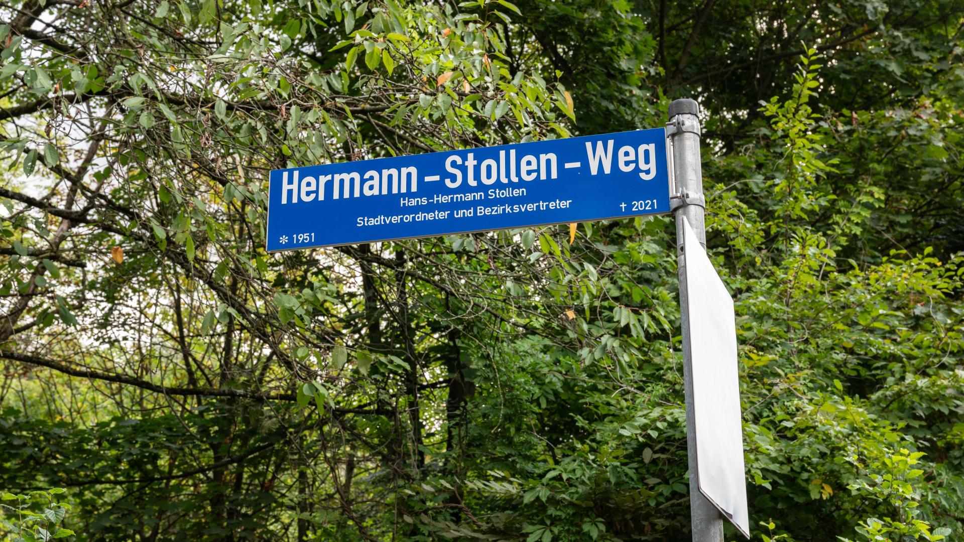 Das Straßennamenschild Hermann-Stollen-Weg ist mit der Erläuterung „Stadtverordneter und Bezirksvertreter, *1951 †2021“ versehen. 