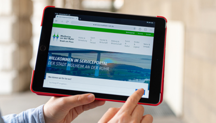 Eine Frau hält ihr Tablet in die Kamera, darauf ist die Startseite des Mülheimer Serviceportals zu sehen