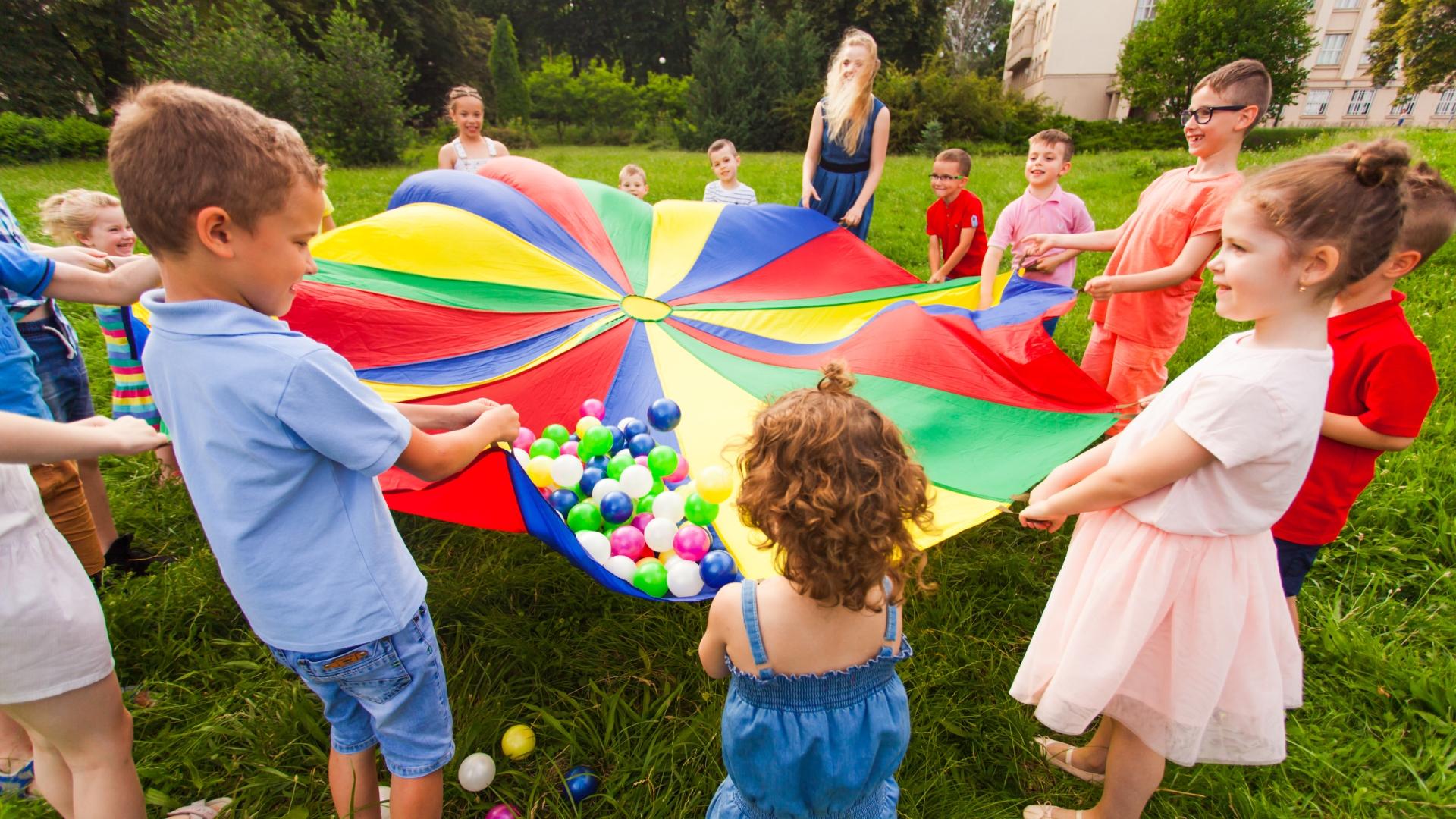 Kinder stehen im Kreis und spielen mit einem bunten Tuch und Bällen