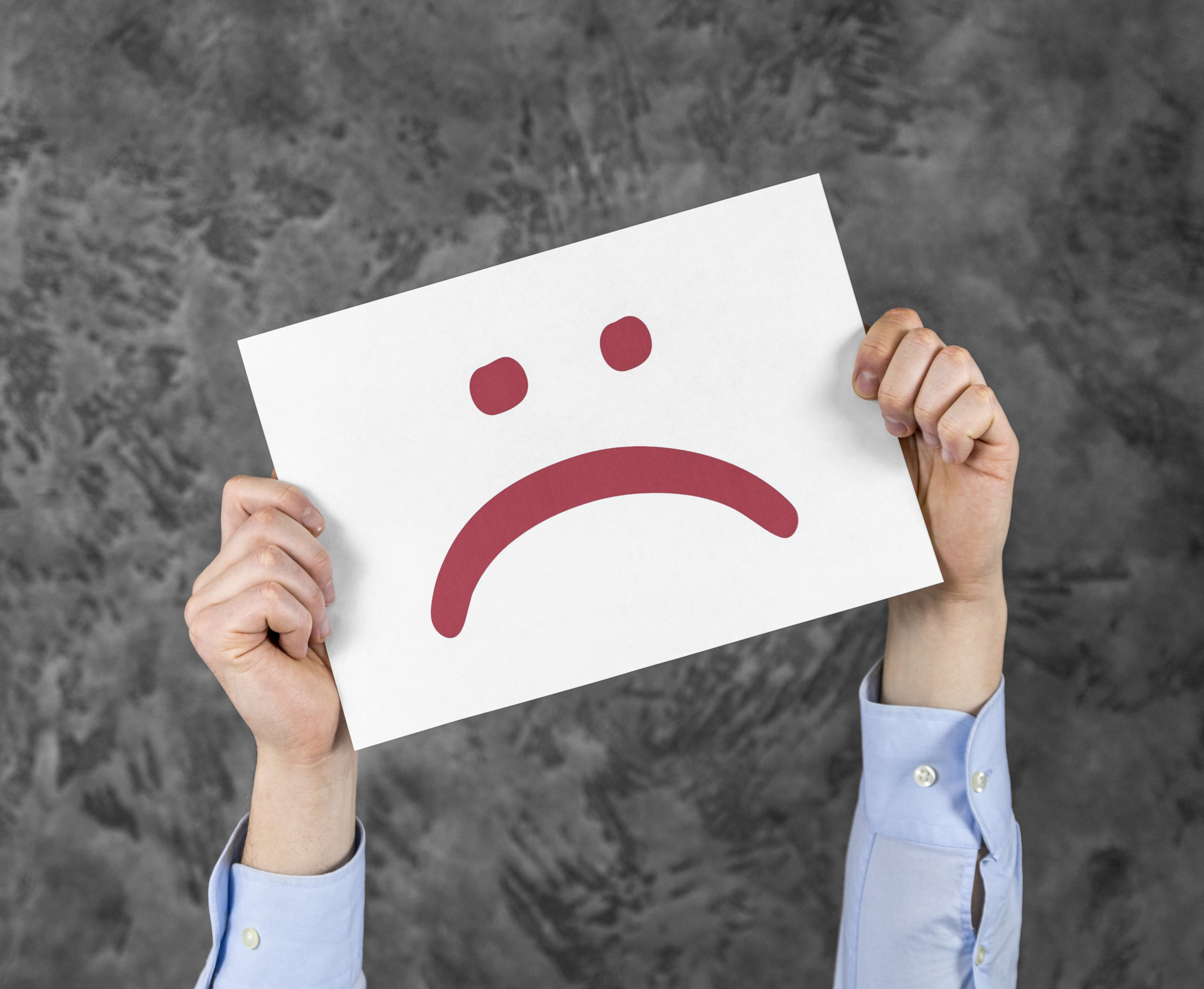 Hände die ein Schild mit einem traurigen Smiley halten
