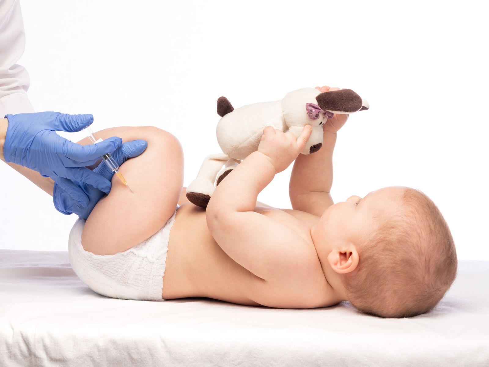 Ein Baby wird beim Arzt geimpft. Es hält dabei ein Stofftier in der Hand.