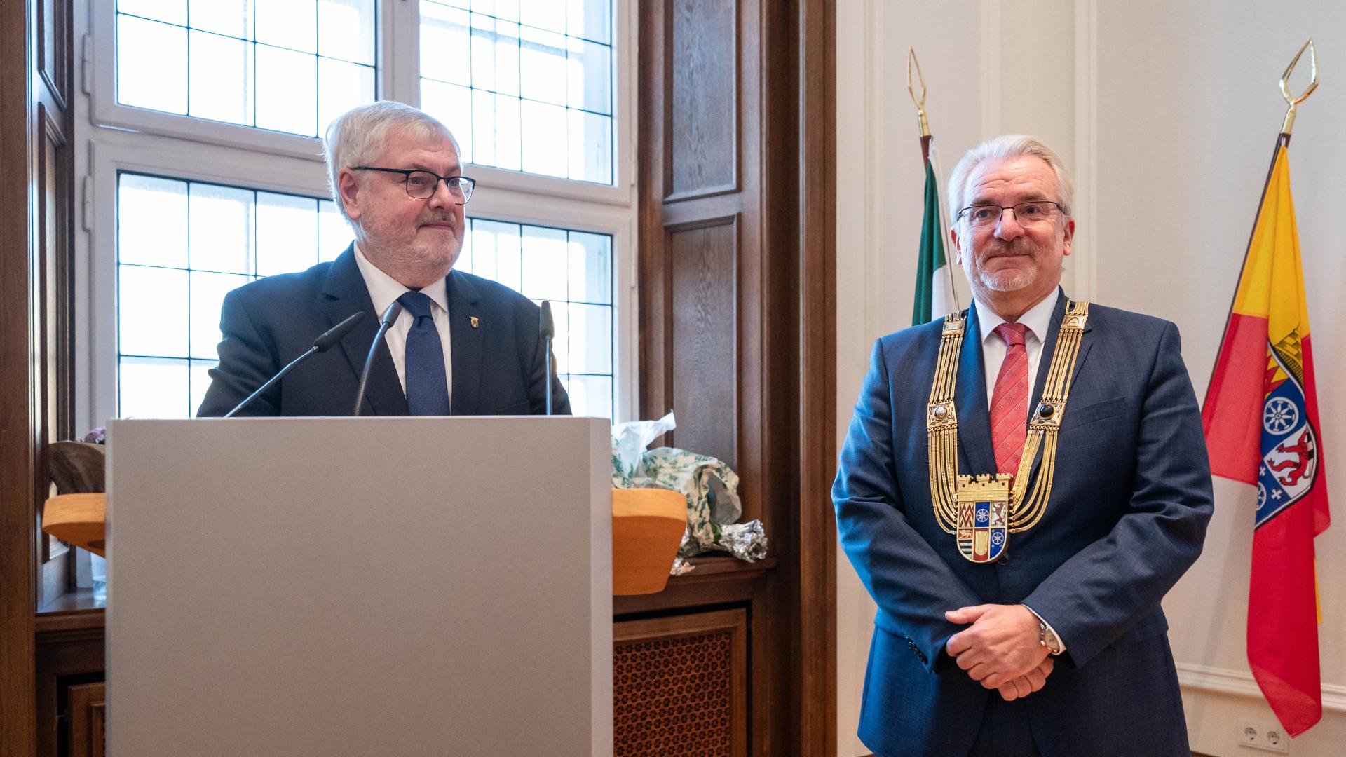 Bürgermeister Markus Püll steht hinter einem Rednerpult. Amtseinführung von Marc Buchholz zum Oberbürgermeister der eine goldene Amtskette trägt und vor der Mülheim Flagge steht.