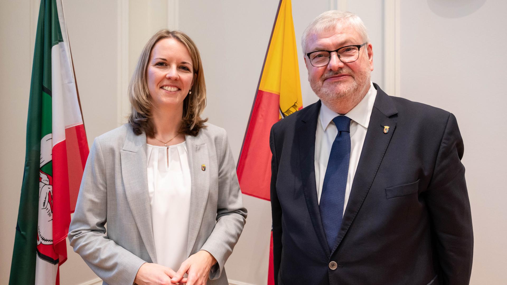 Ehrenamtliche Stellvertreterin Alexandra Hanf und Stellvertreter Markus Püll stehen vor der Mülheim Flagge im Ratssaal. 