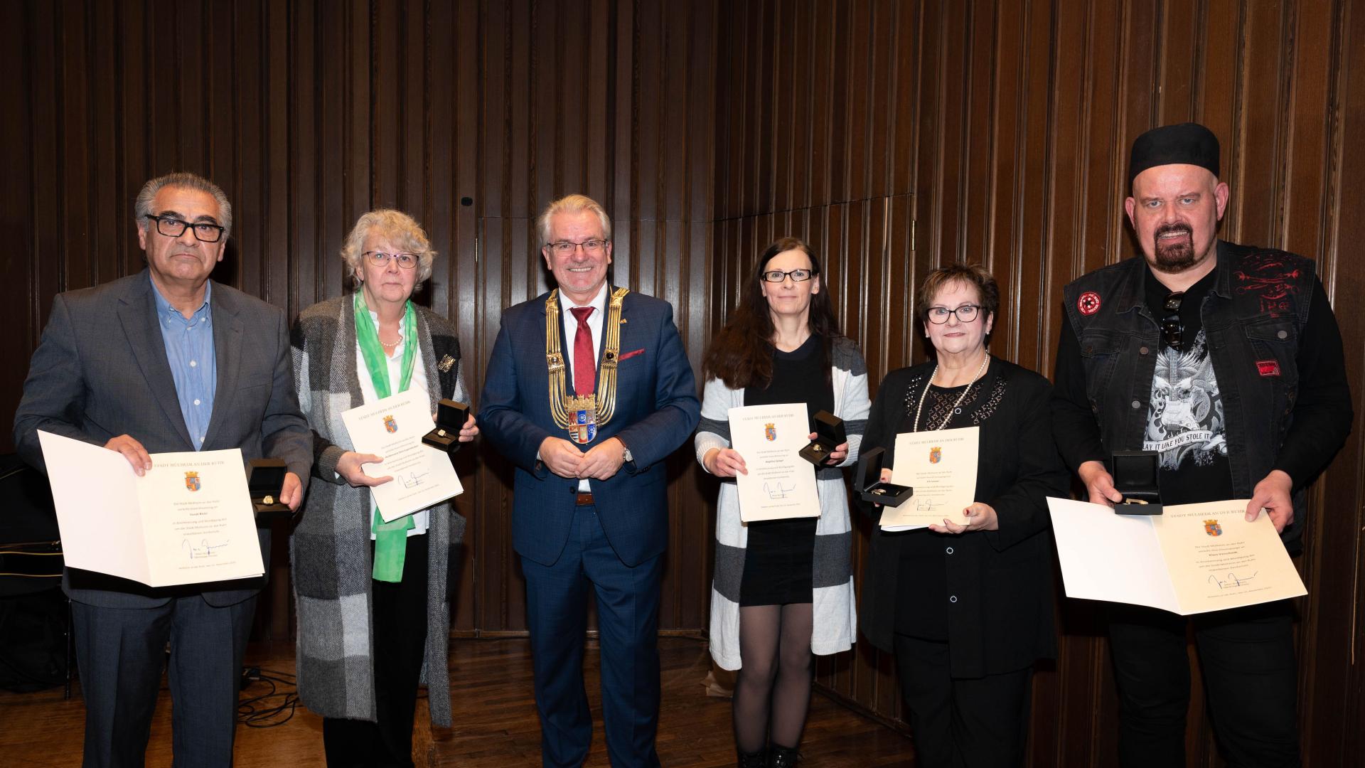 Die fünf ausgezeichneten Frauen und Männer haben sich für ein Gruppenfoto aufgestellt und halten ihre Urkunden, Ehrenspangen und Ehrenringe in die Kamera. In der Mitte steht der Oberbürgermeister mit seiner Amtskette.
