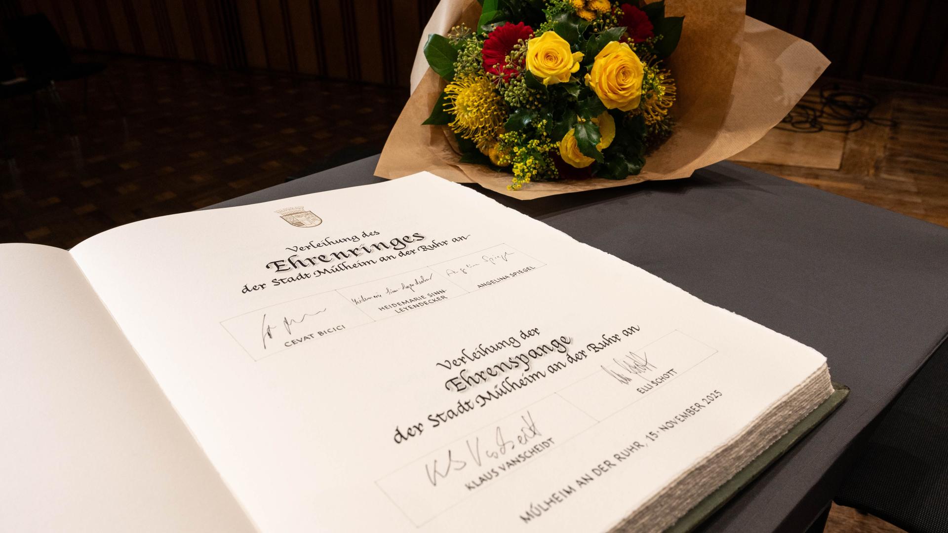 Blick in das Goldene Buch der Stadt mit den Unterschriften der aktuellen Trägerinnen und Träger von Ehrenspange und Ehrenring. Im Hintergrund ein Blumenstrauß.