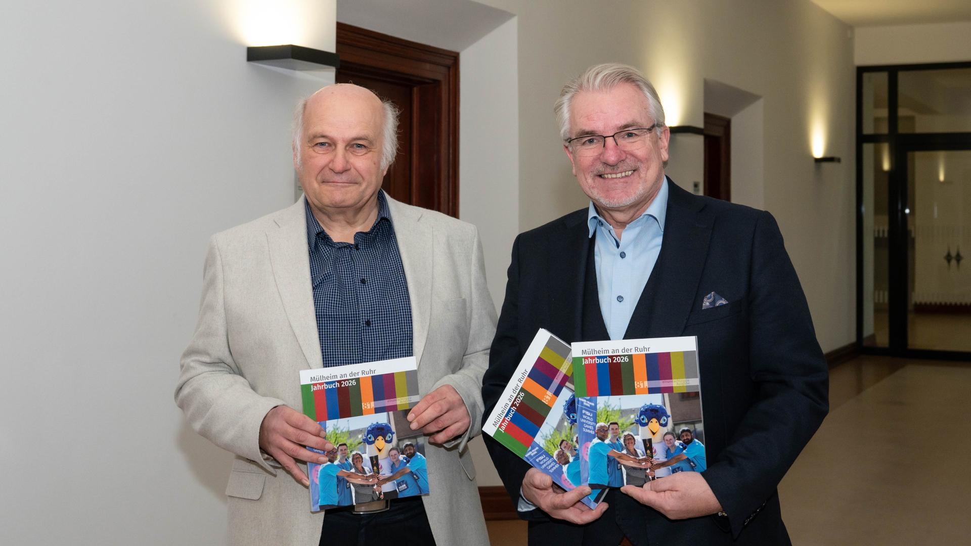 Hansgeorg Schiemer und Oberbürgermeister Marc Buchholz stehen in einem Flur und halten jeweils mehrere Jahrbücher in den Händen.