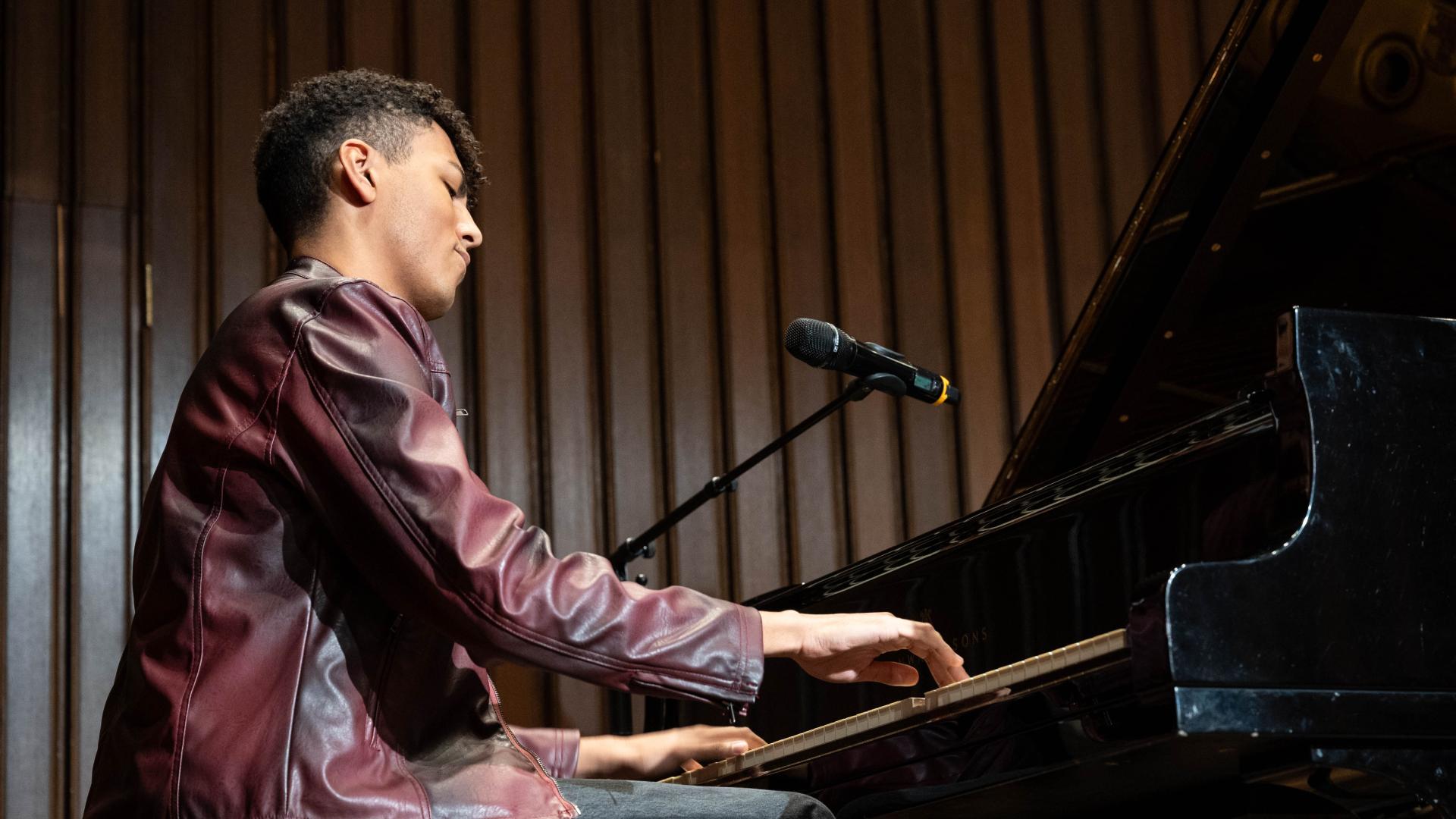 Louis Philippson in Lederjacke spielt Klavier, Mikrofon steht auf einem Ständer neben dem Instrument.