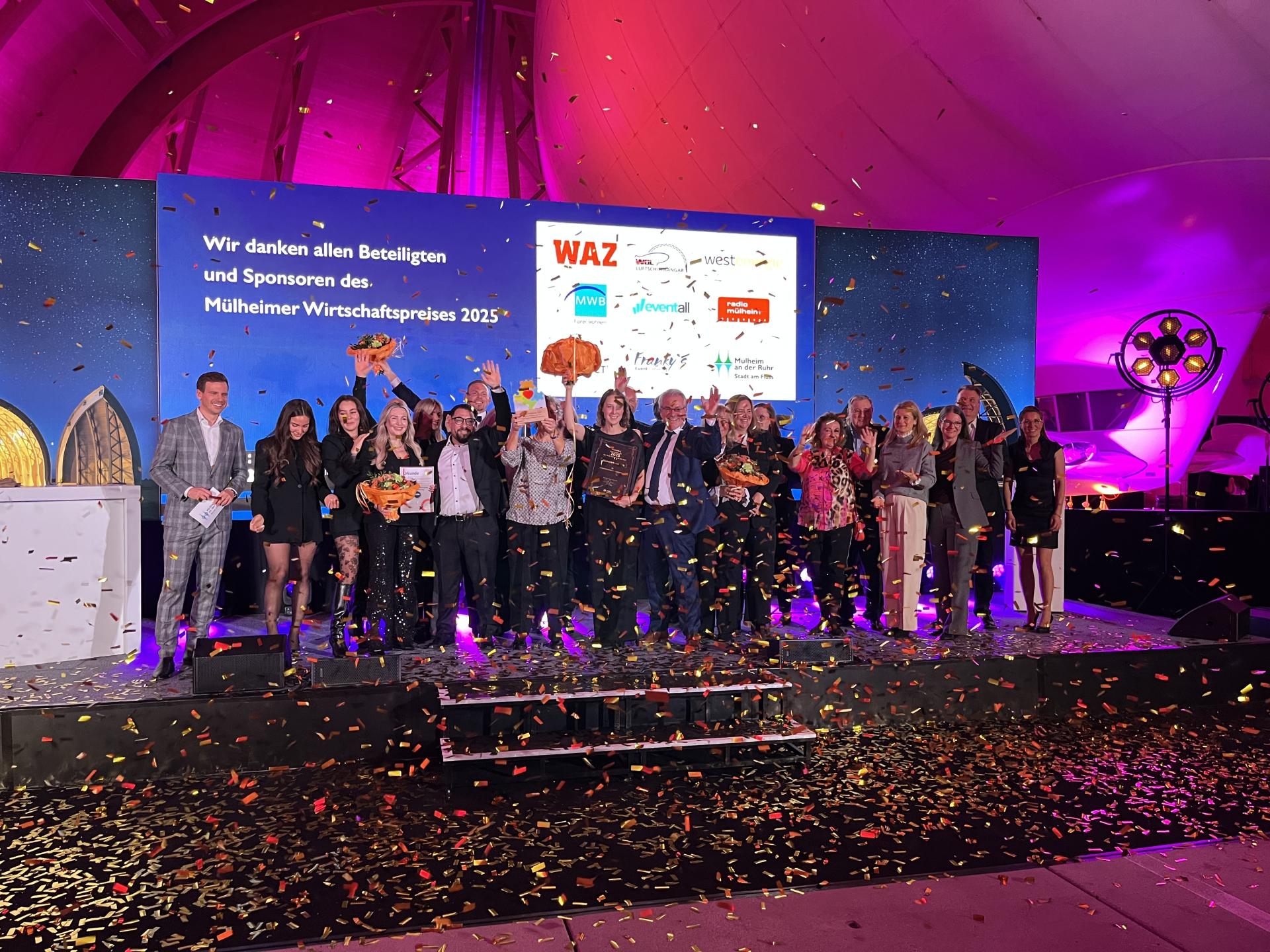 Gewinner, Nominierte und Beteiligte des Mülheimer Wirtschaftspreises stehen auf einer Bühne im goldenen Konfetti-Regen.