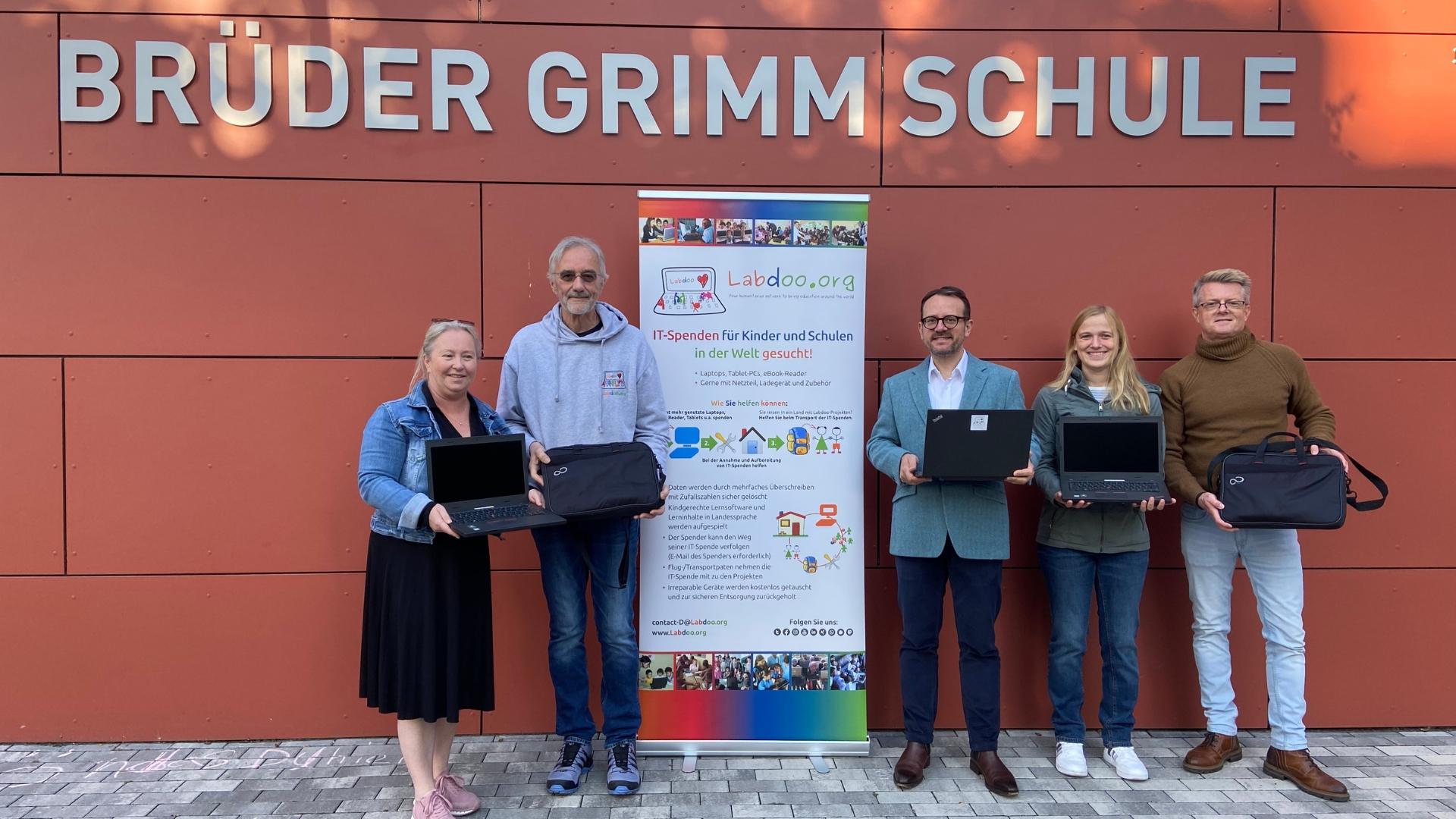 Gruppenfoto vor der Brüder Grimm Schule in Mülheim. Fünf Erwachsene halten Laptops in der Hand.